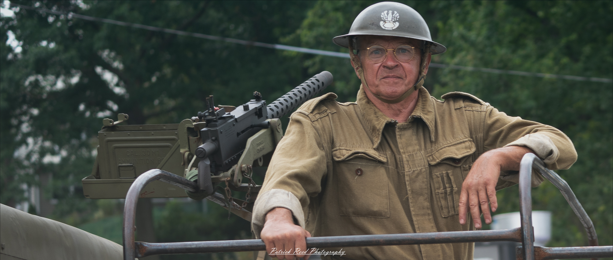 A soldier on a truck, with a .50 caliber machine gun mounted in the background. The image reflects readiness and strength, highlighting the soldier’s role in a heavily armed convoy, prepared for action.